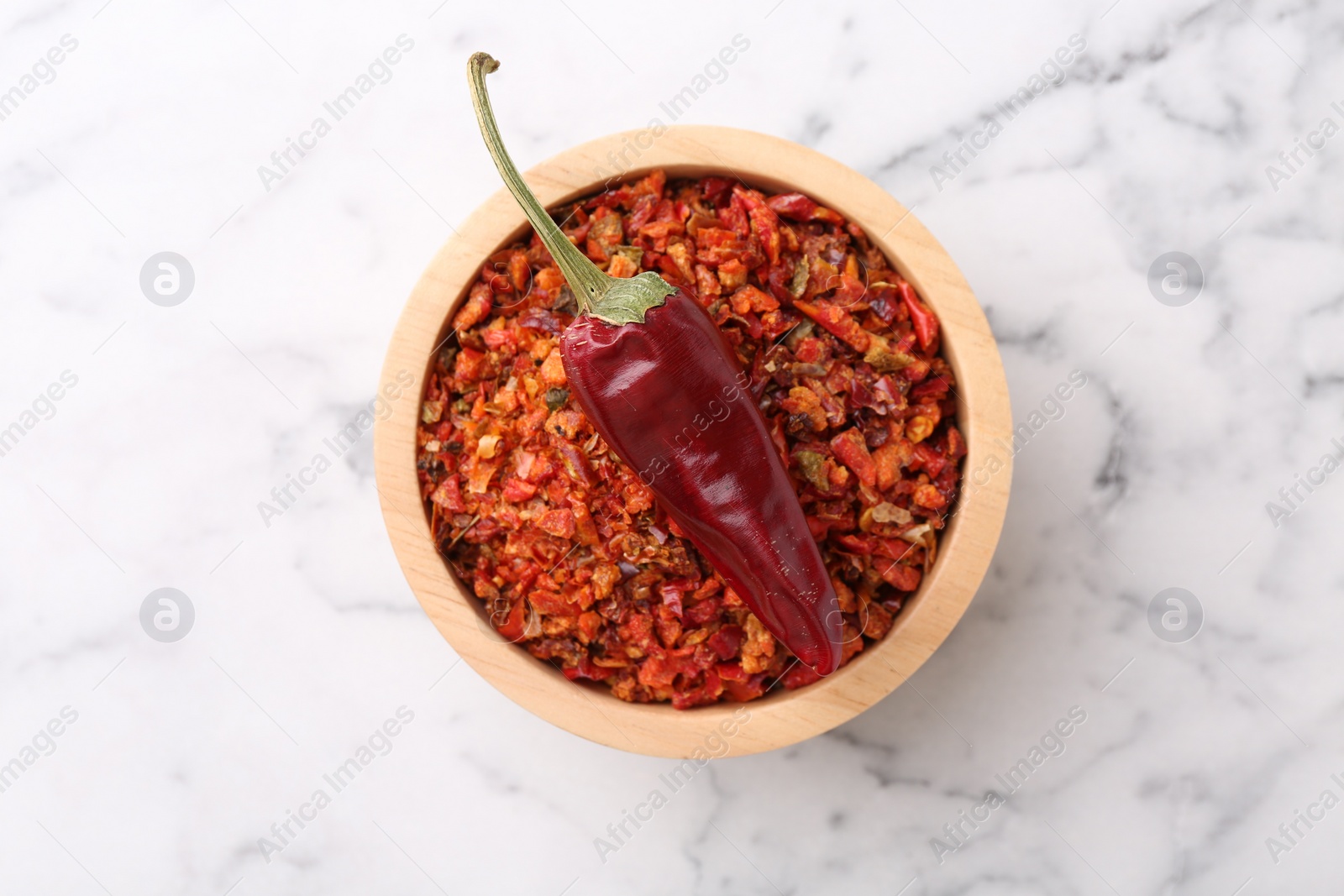 Photo of Chili pepper flakes in bowl and pod on white marble table, top view