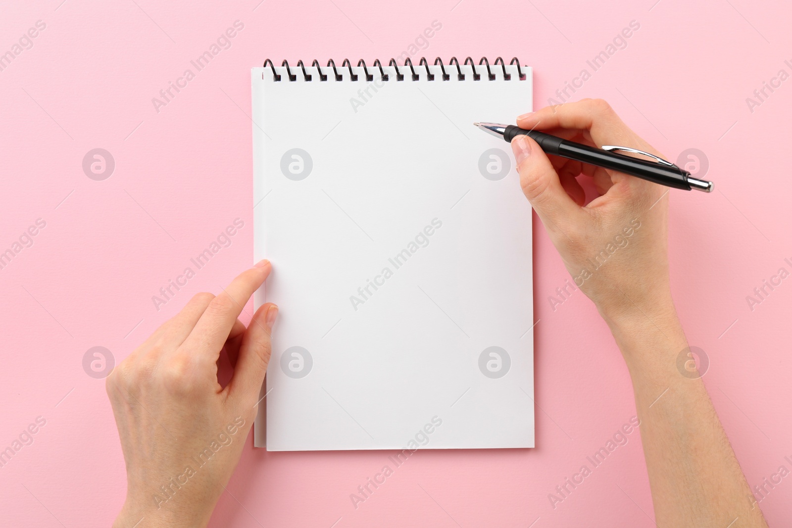 Photo of Woman writing in notebook on pink background, top view