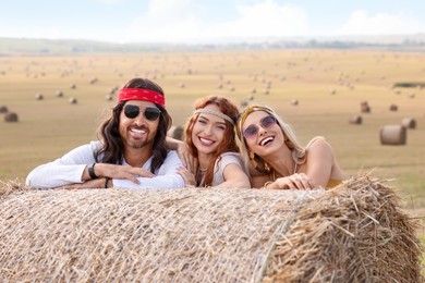 Happy hippie friends near hay bale in field