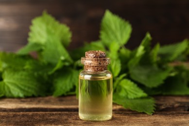 Glass bottle of nettle oil with leaves on wooden table, closeup