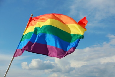 Photo of Bright rainbow gay flag fluttering against blue sky. LGBT community