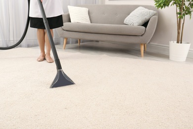 Photo of Chambermaid removing dirt from carpet with vacuum cleaner indoors, closeup. Space for text