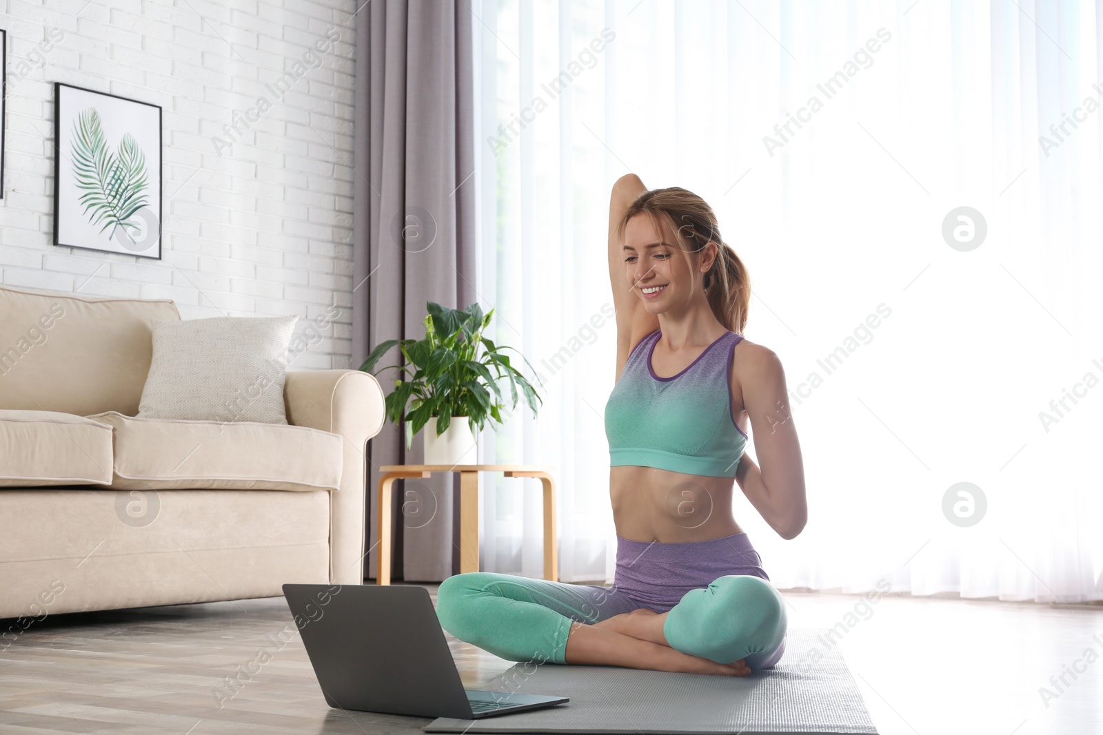 Photo of Woman having online video class via laptop at home. Distance yoga course during coronavirus pandemic