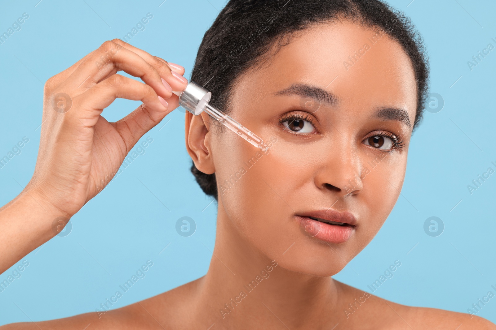 Photo of Beautiful woman applying serum onto her face on light blue background, closeup