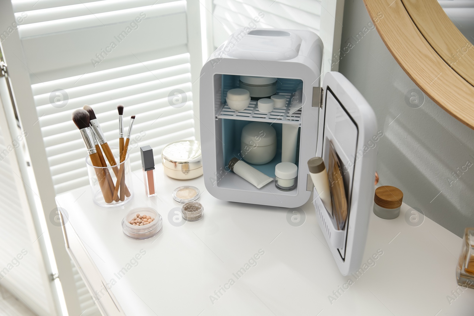 Photo of Cosmetics refrigerator and skin care products on white vanity table indoors