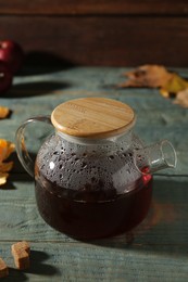 Glass teapot with hot beverage on light blue wooden table