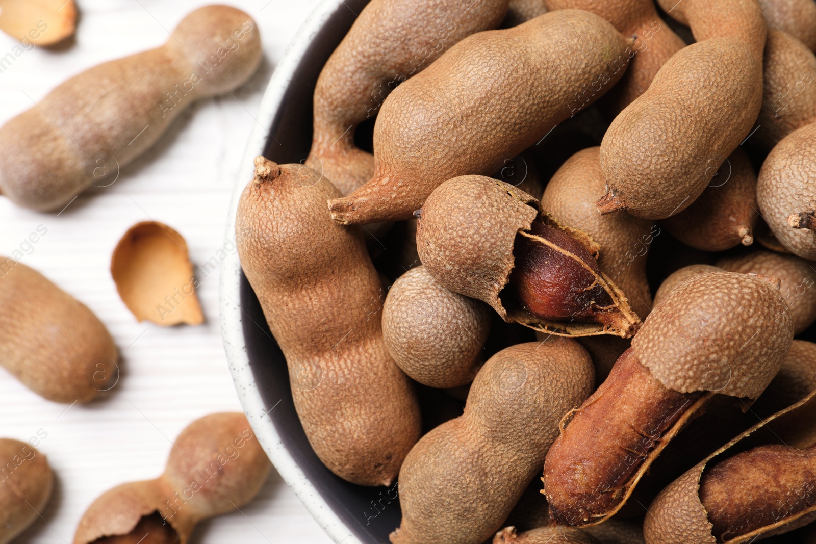 Photo of Delicious ripe tamarinds in bowl on white table, closeup