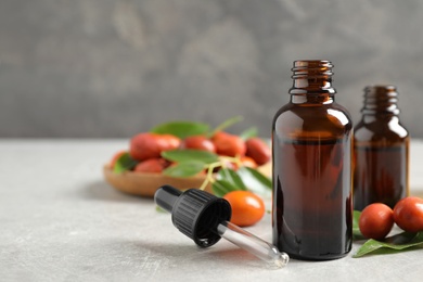 Glass bottles with jojoba oil and seeds on stone table against grey background. Space for text