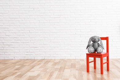 Photo of Stuffed toy rabbit on chair in child room. Space for text