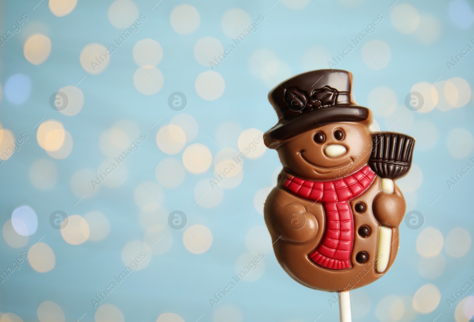 Photo of Funny chocolate snowman candy against blurred festive lights, closeup. Space for text