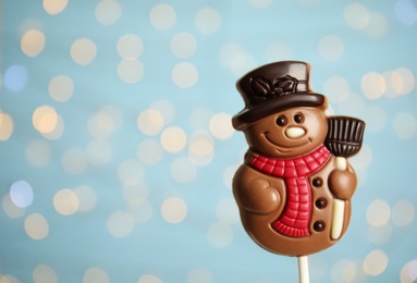 Funny chocolate snowman candy against blurred festive lights, closeup. Space for text