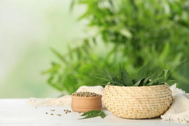 Photo of Bowls with hemp leaves and seeds on table against blurred background