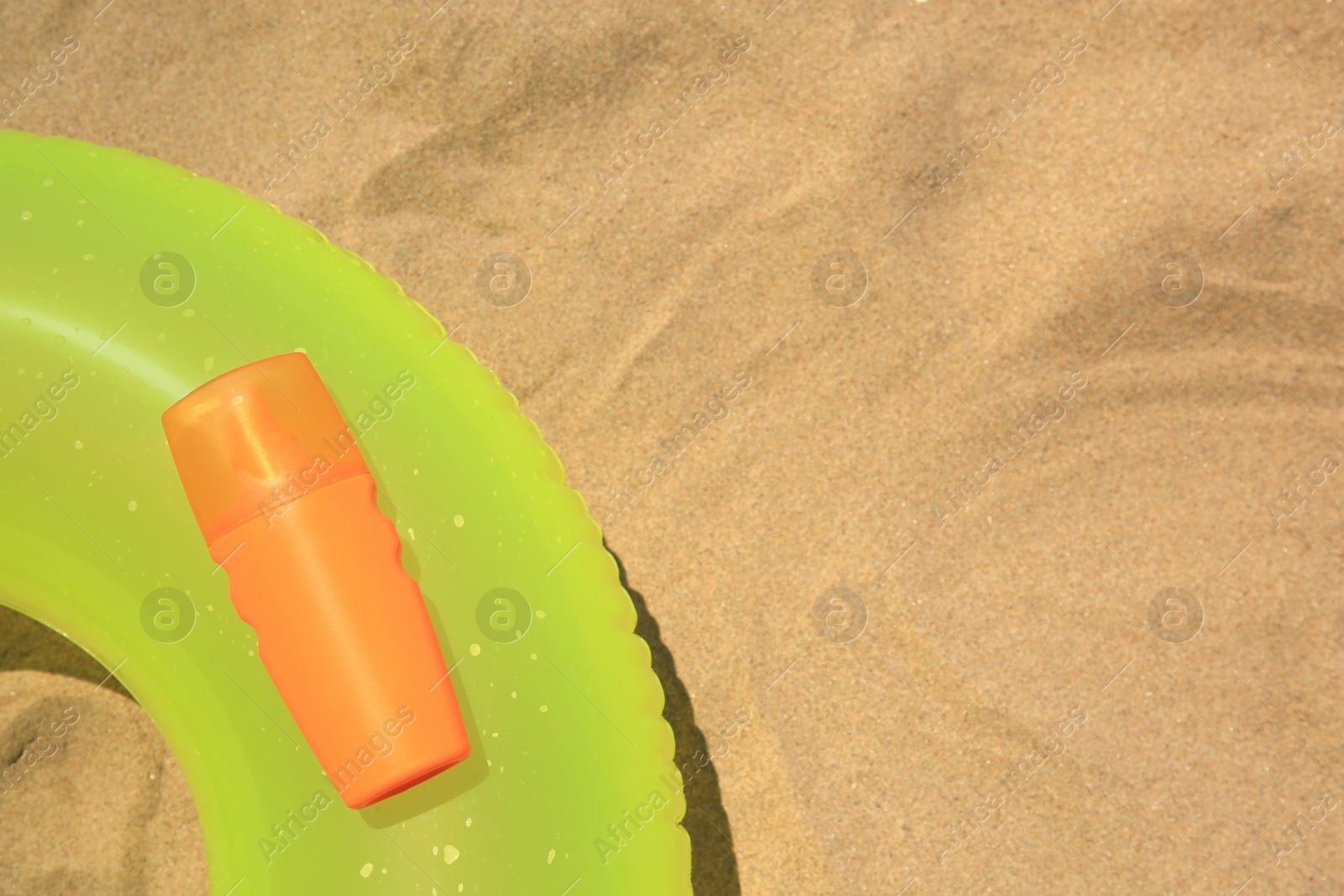 Photo of Sunscreen and inflatable ring on sand, top view with space for text. Sun protection care