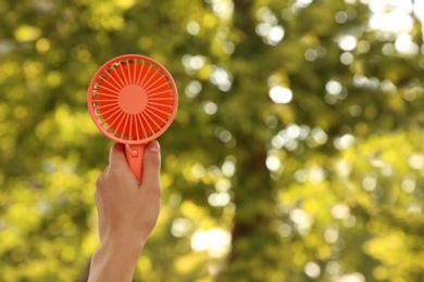 Woman holding portable fan outdoors on sunny summer day, closeup. Space for text