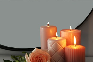 Burning candles and rose near mirror in room, closeup. Space for text