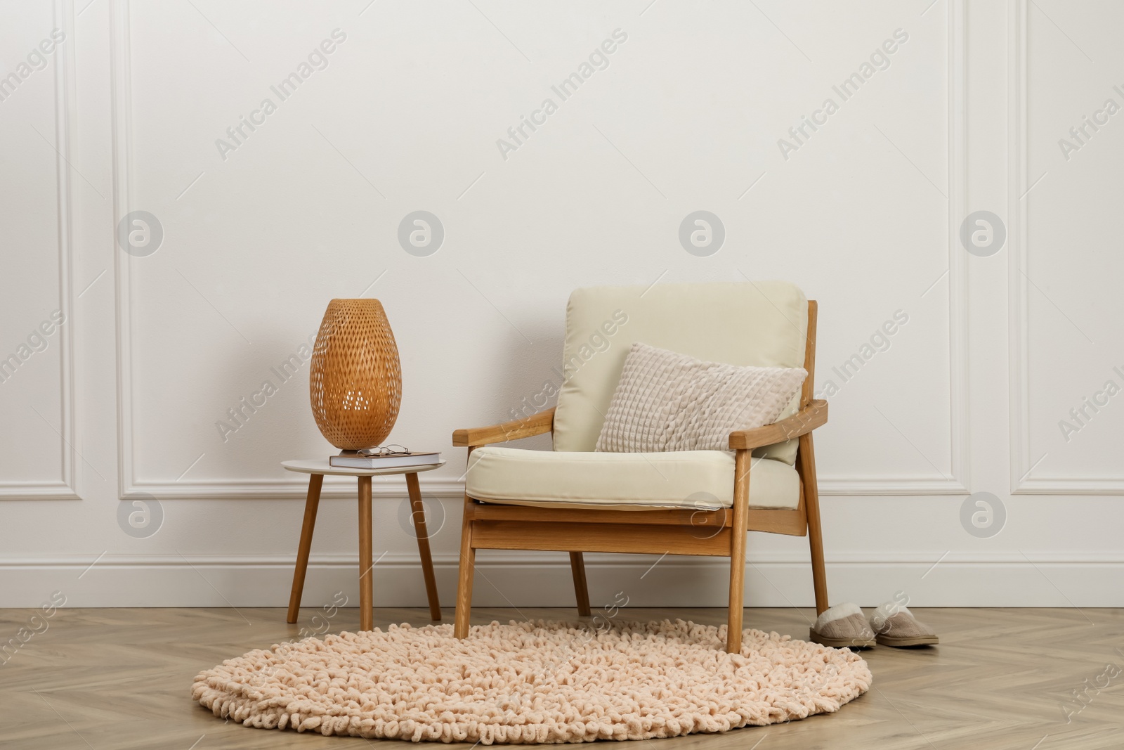 Photo of Stylish armchair with cushion and lamp near white wall indoors. Interior design