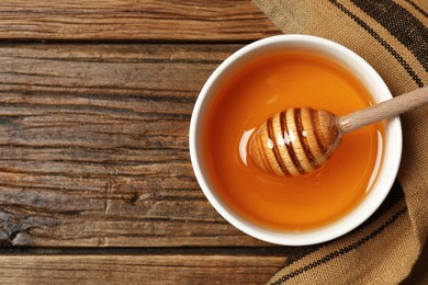 Photo of Bowl with tasty honey and dipper on wooden table, top view. Space for text