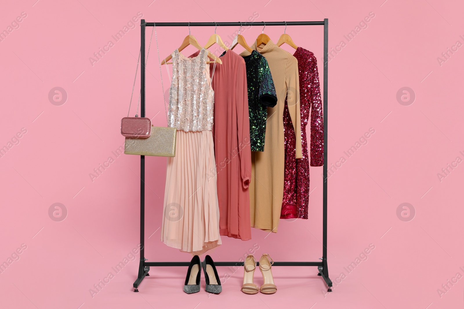 Photo of Rack with stylish women's clothes on wooden hangers, accessories and shoes against pink background