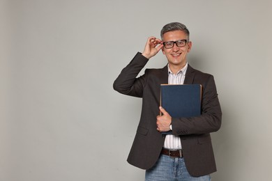 Teacher in glasses holding notebooks on grey background, space for text