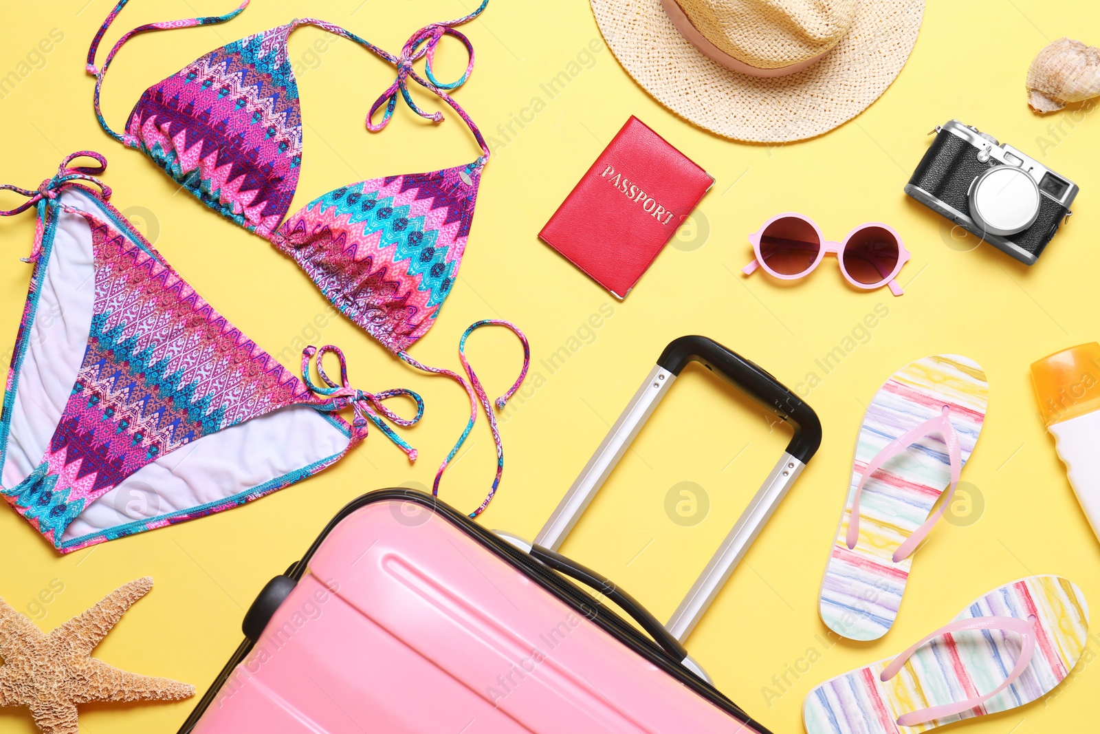 Photo of Flat lay composition with suitcase and beach objects on yellow background