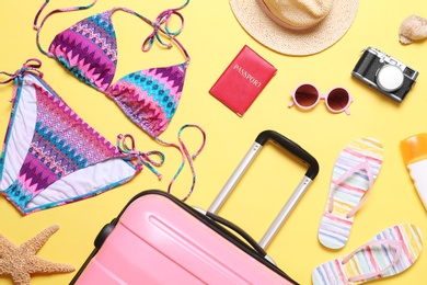 Photo of Flat lay composition with suitcase and beach objects on yellow background