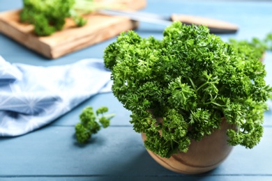 Photo of Fresh curly parsley in wooden bowl on blue table