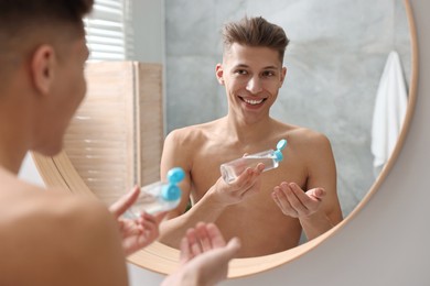 Photo of Handsome man with bottle of lotion in bathroom