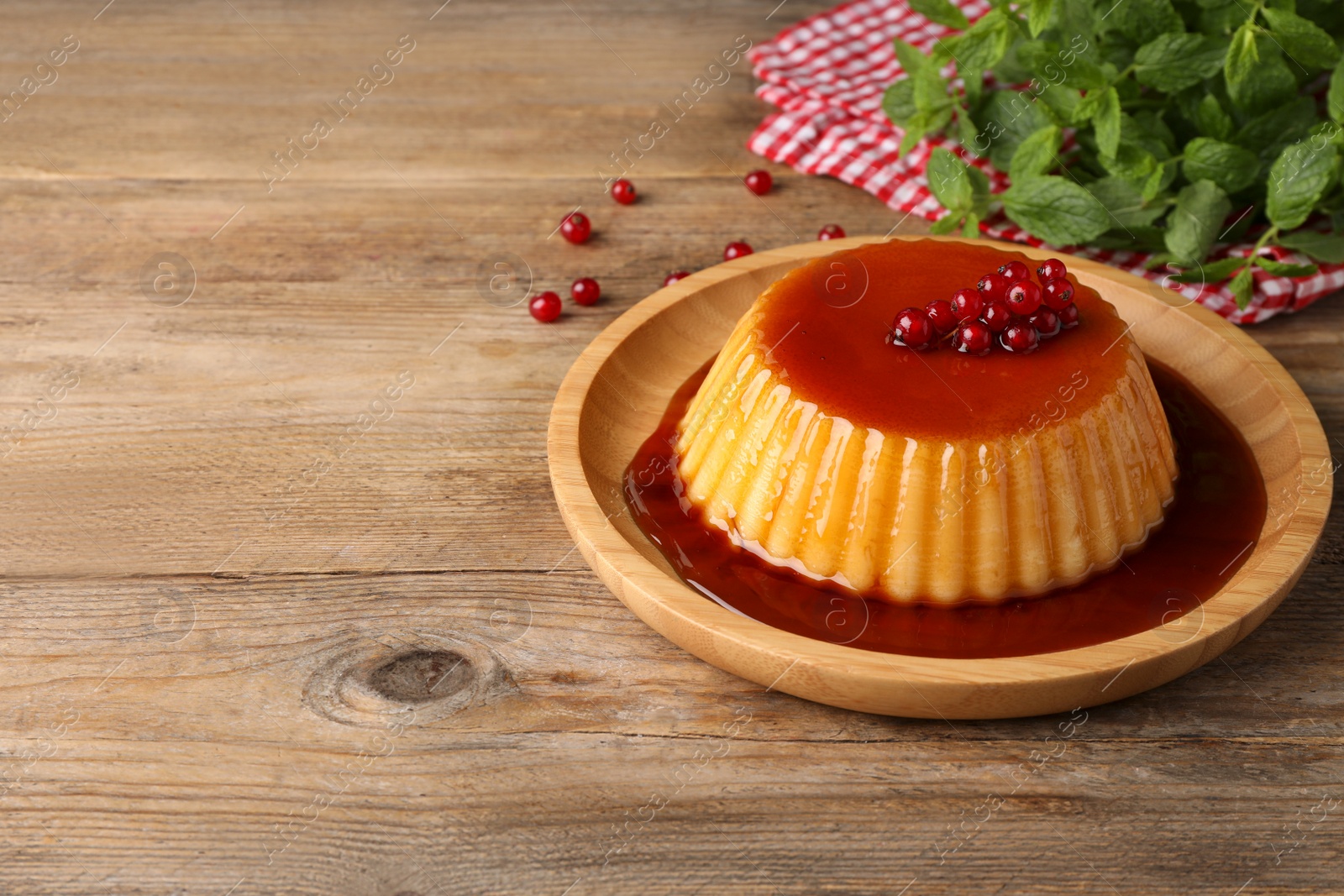 Photo of Delicious pudding with caramel and redcurrants on wooden table. Space for text