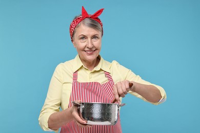 Happy housewife with pot on light blue background