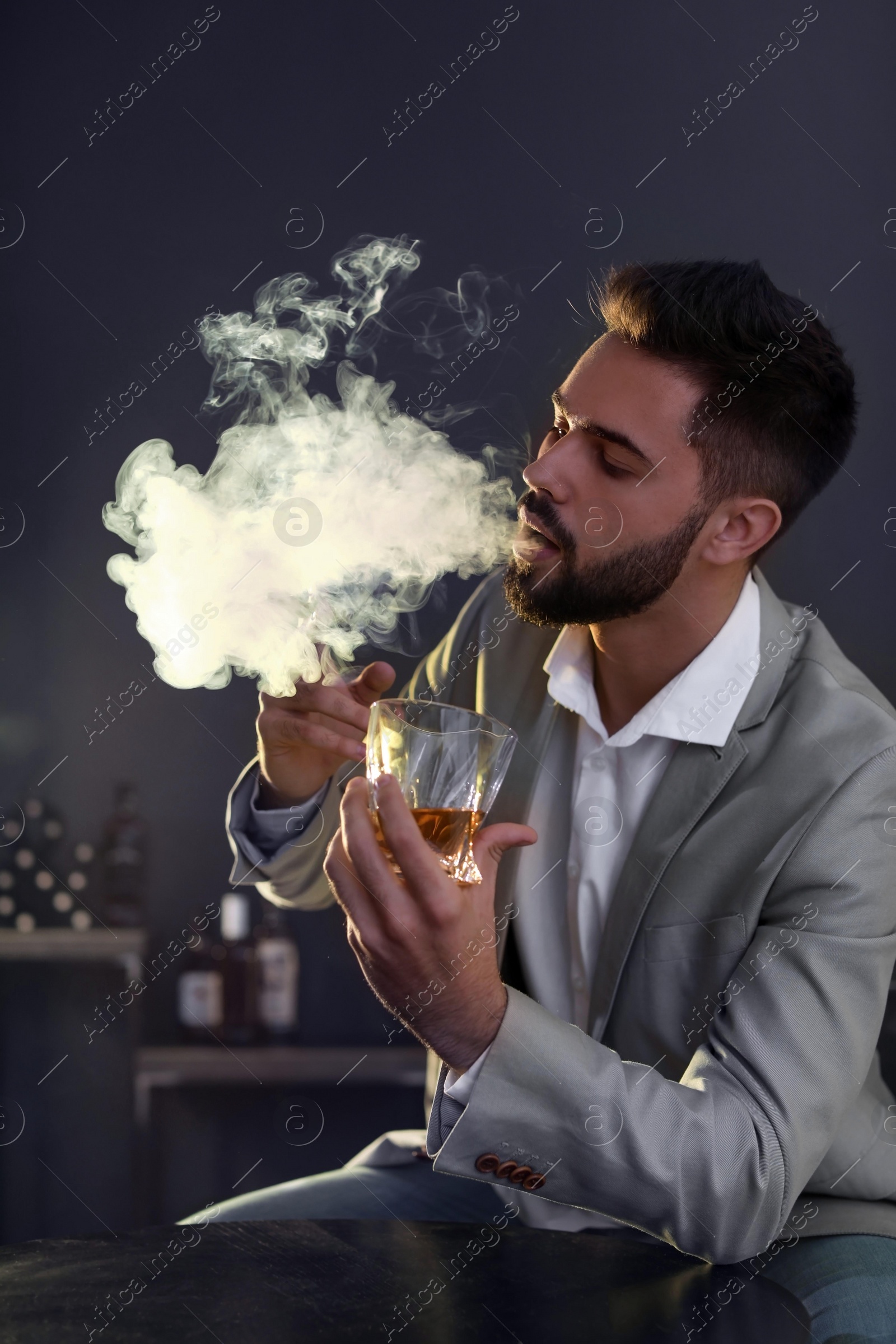 Photo of Man with glass of whiskey and cigar sitting at table indoors