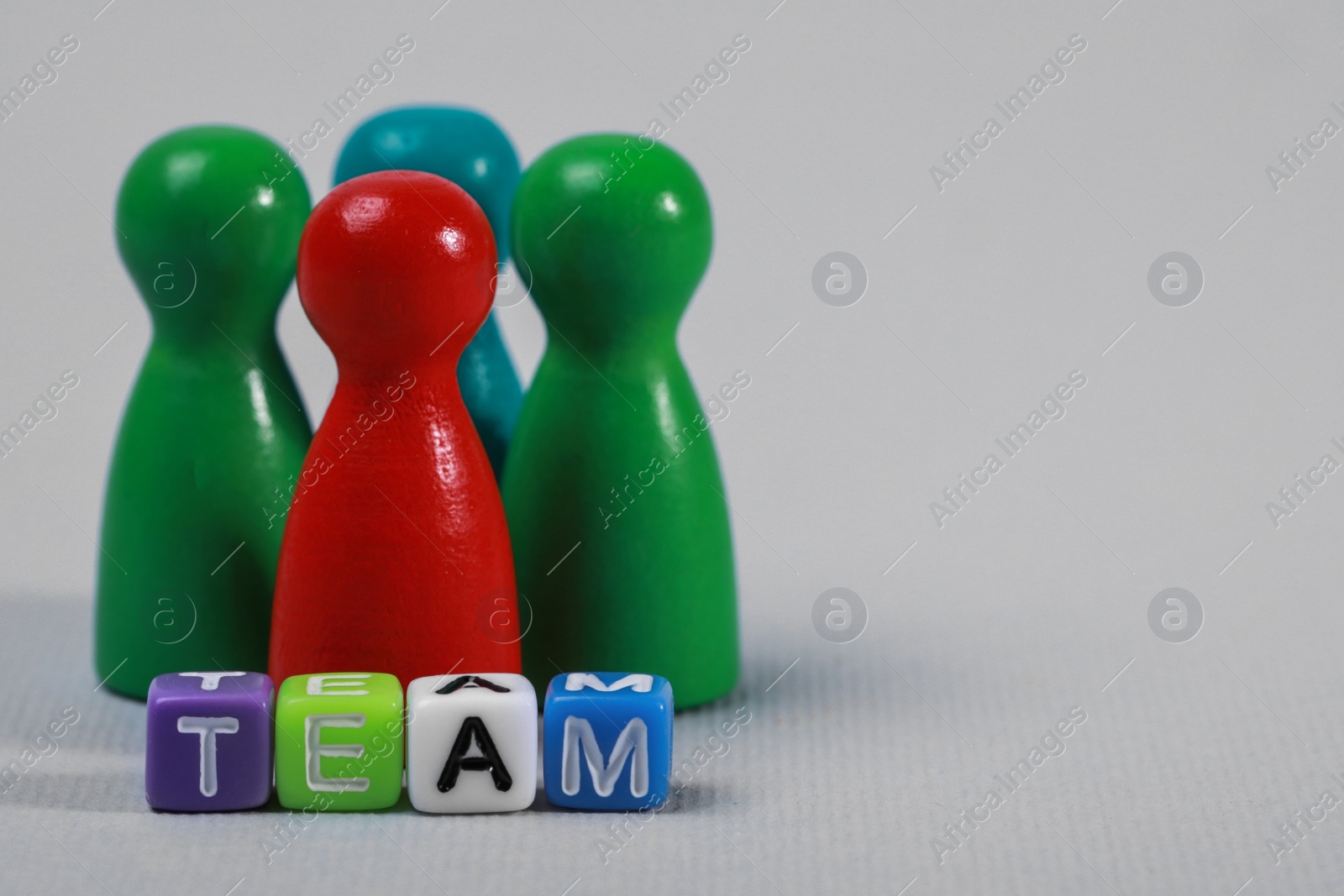 Photo of Colorful pawns and cubes with word Team on light grey background, closeup with space for text. Recruiter searching employee
