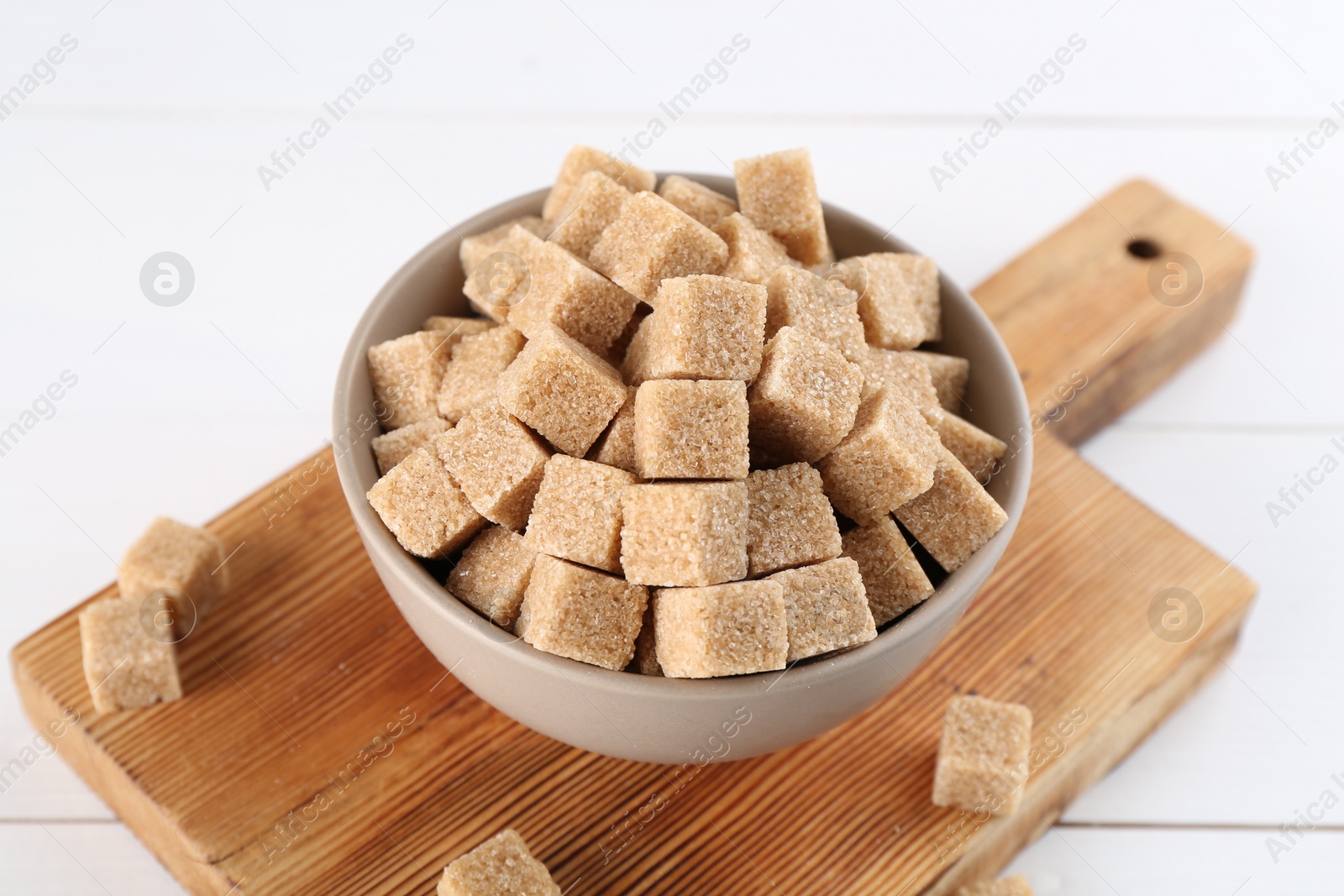 Photo of Brown sugar cubes in bowl on white table, closeup