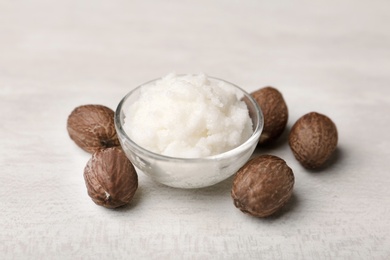 Shea butter in bowl and nuts on white table