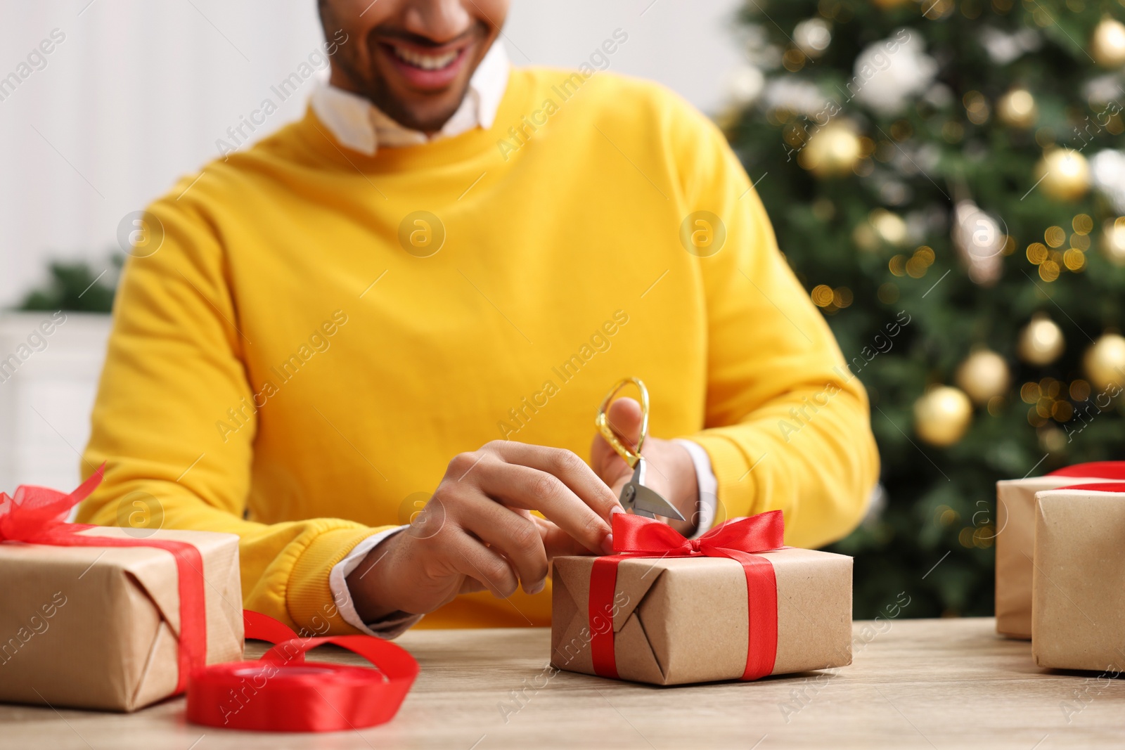 Photo of Man decorating Christmas gift box at wooden table indoors, closeup