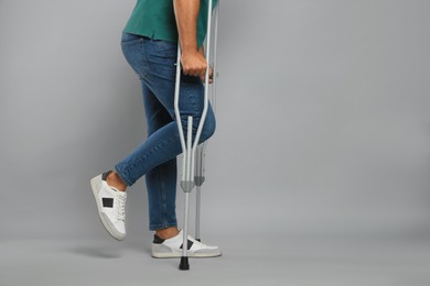 Photo of Young man with axillary crutches on grey background, closeup. Space for text