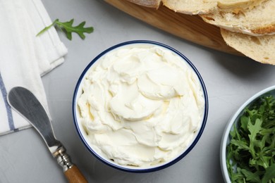 Tasty cream cheese, fresh bread and arugula on grey table, flat lay