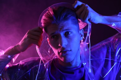 Photo of Young man wearing clear coat in neon lights with smoke effect