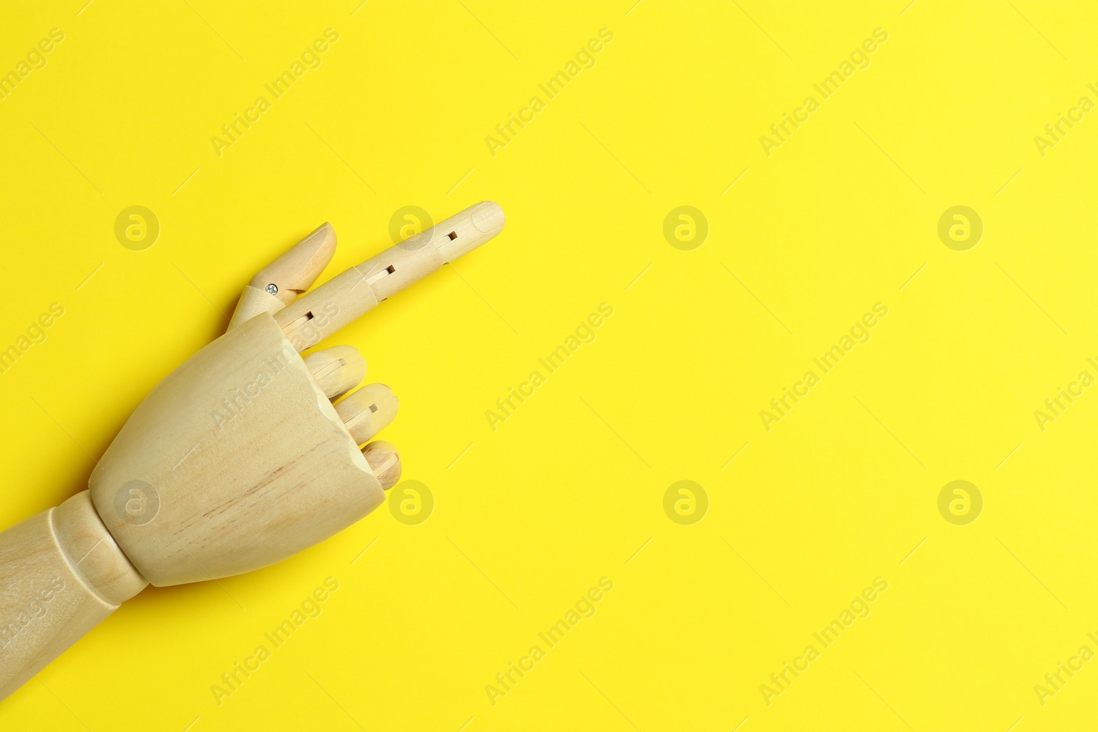 Photo of Wooden mannequin hand on yellow background, top view. Space for text