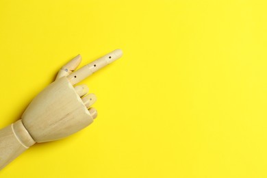 Wooden mannequin hand on yellow background, top view. Space for text