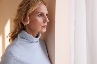 Photo of Upset middle aged woman near window at home. Loneliness concept