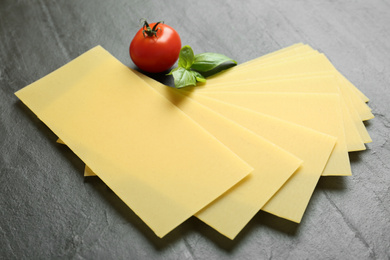 Photo of Uncooked lasagna sheets, tomato and basil on dark background