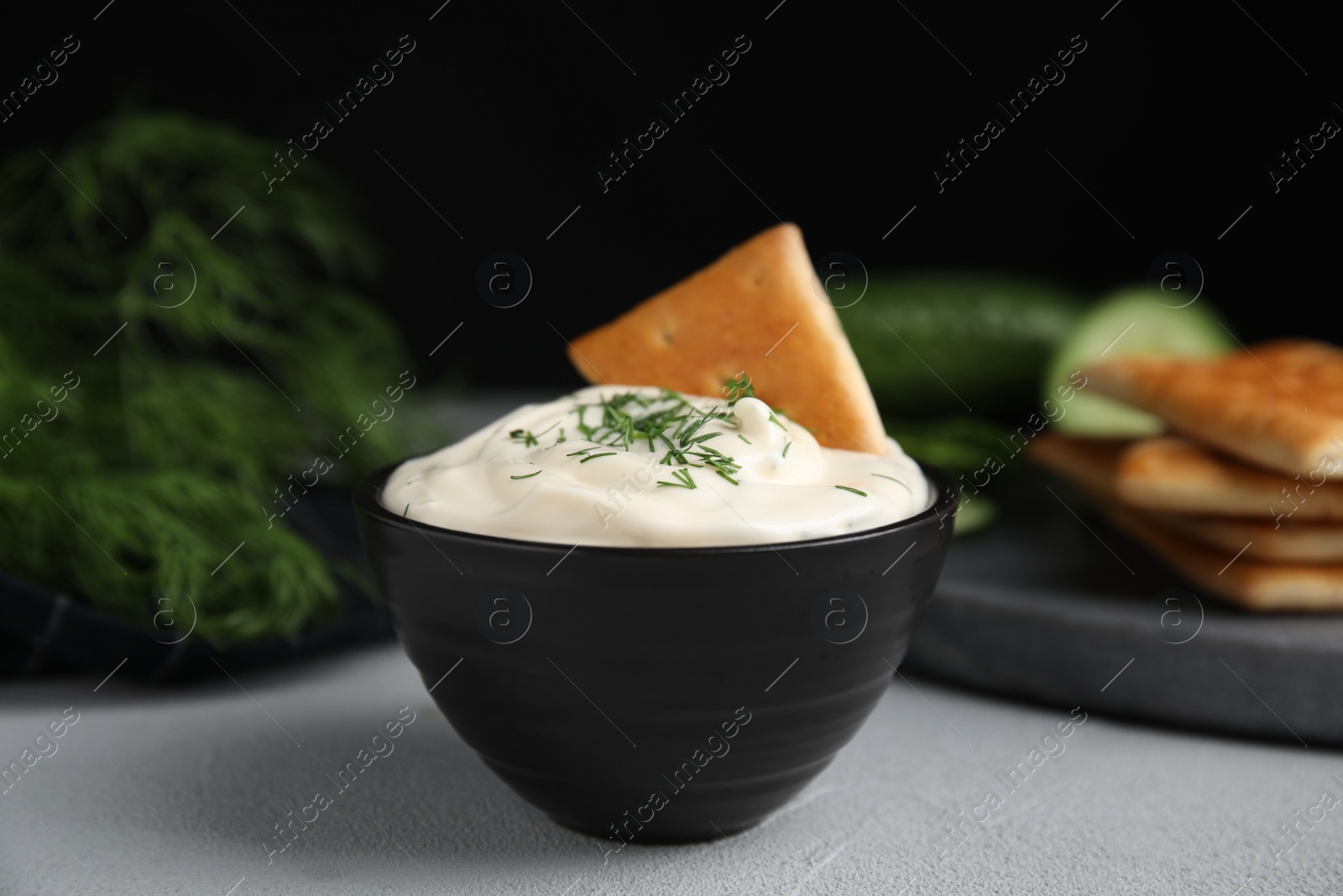 Photo of Tasty creamy dill sauce with cracker in bowl on grey table, closeup