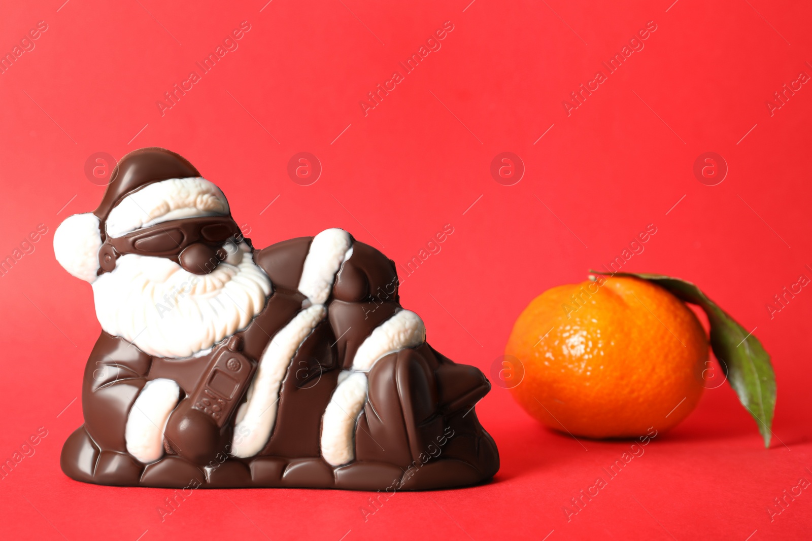 Photo of Chocolate Santa Claus and tangerine on red background