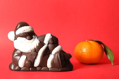 Photo of Chocolate Santa Claus and tangerine on red background