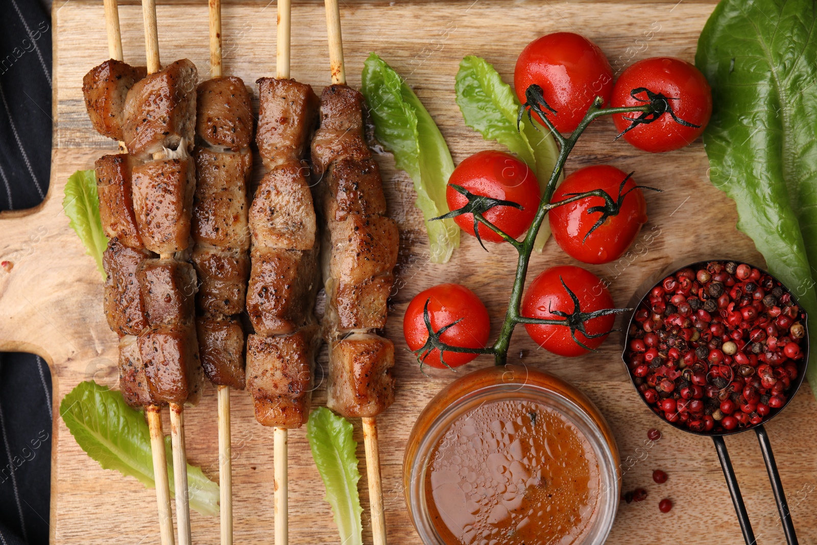 Photo of Tasty cooked marinated meat served with sauce and tomatoes on wooden table, flat lay