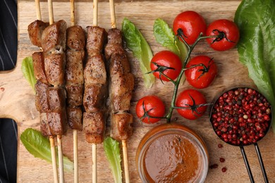 Photo of Tasty cooked marinated meat served with sauce and tomatoes on wooden table, flat lay