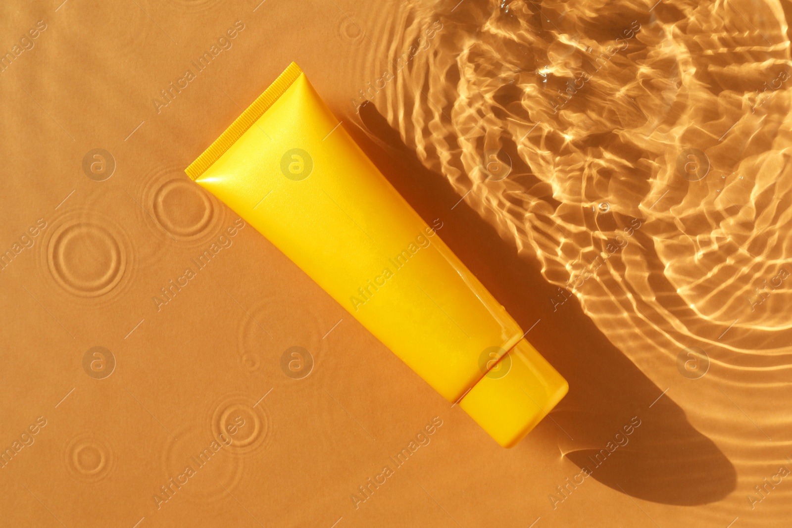 Photo of Tube with moisturizing cream in water on orange background, top view