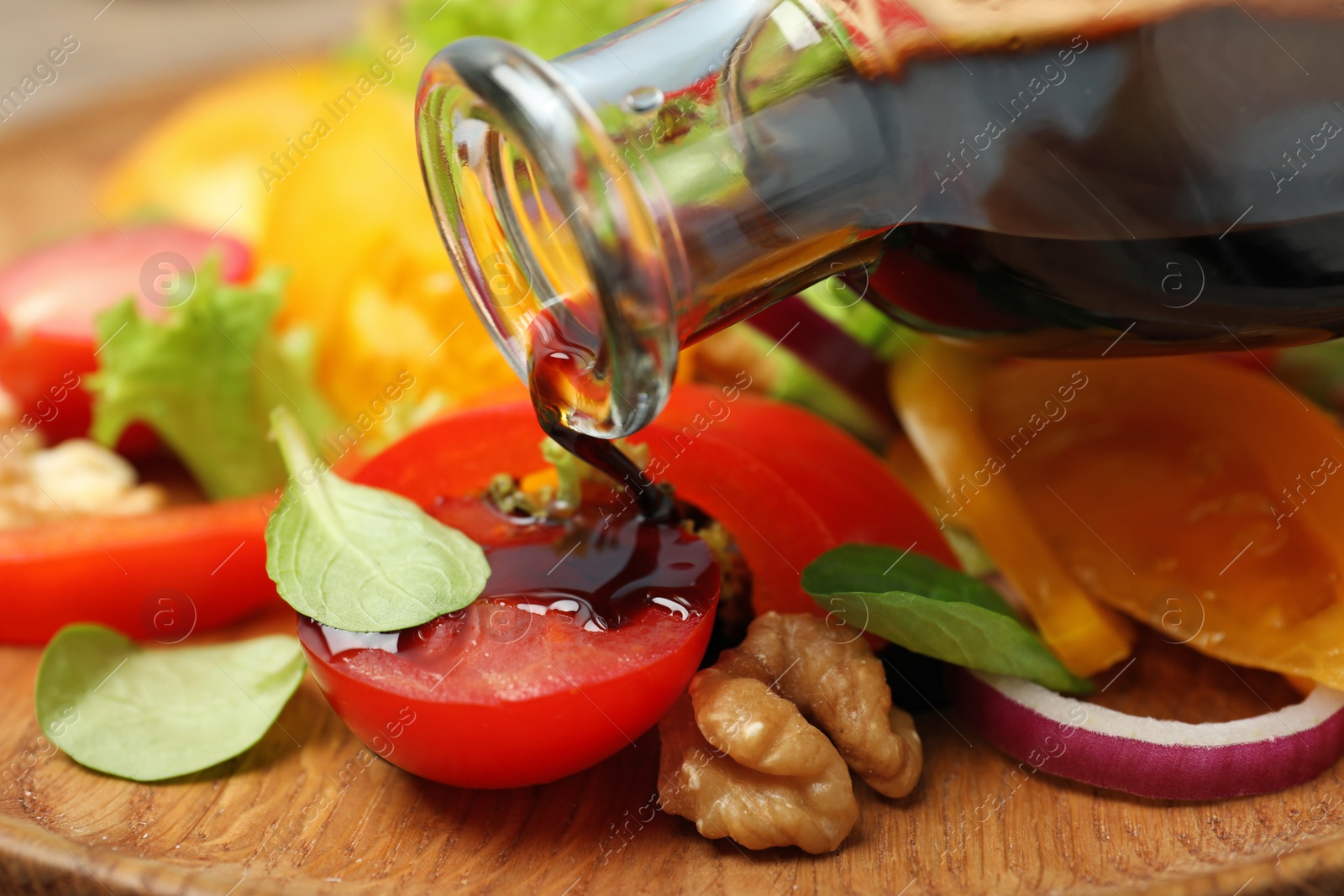 Photo of Pouring balsamic vinegar onto fresh vegetable salad, closeup