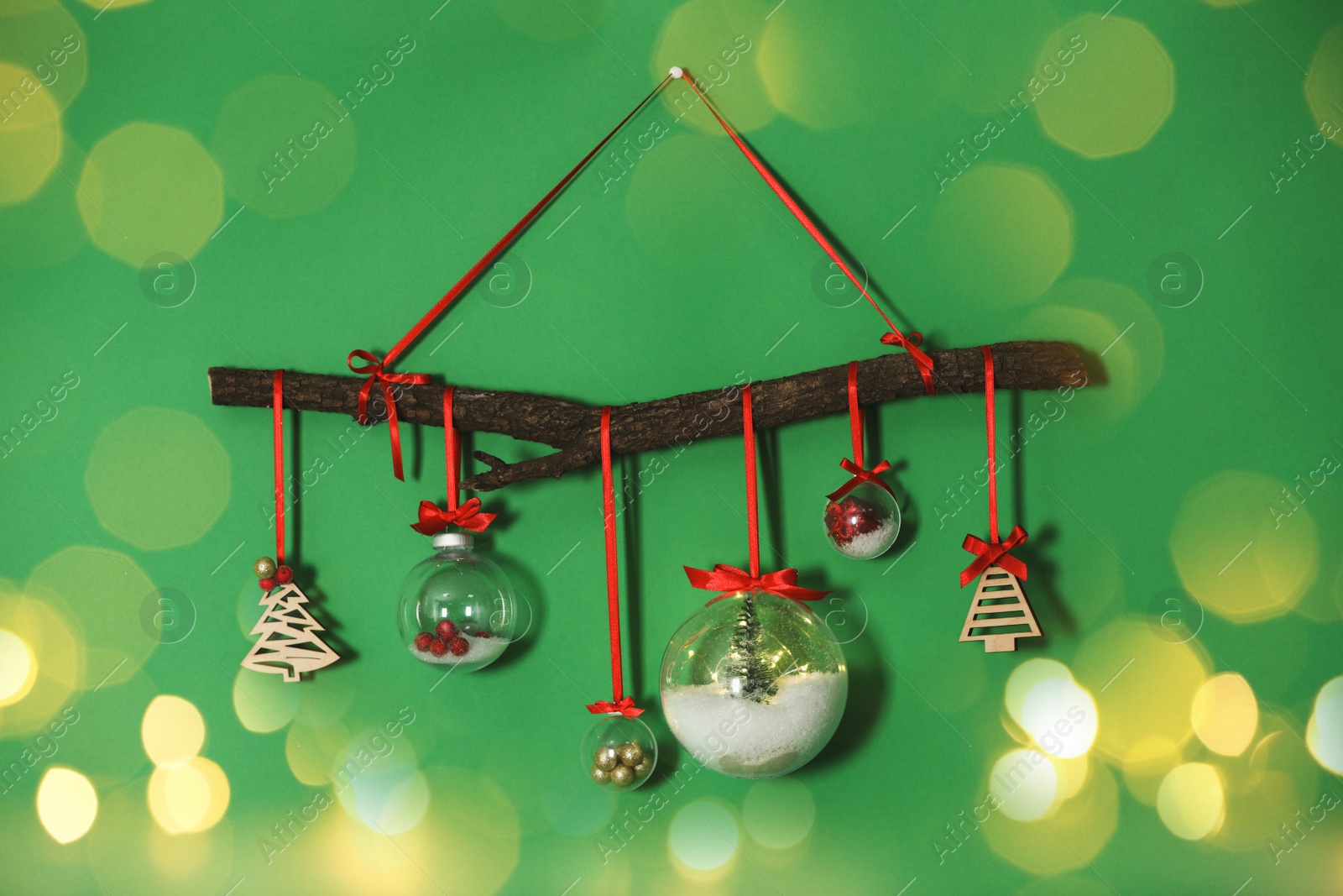 Image of Beautiful Christmas decoration of tree branch and holiday ornaments hanging on green wall, bokeh effect