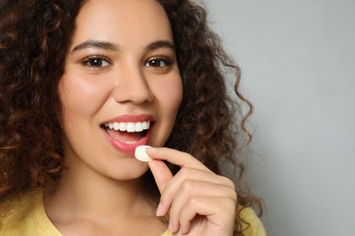 Photo of African-American woman taking vitamin pill on light grey background, closeup